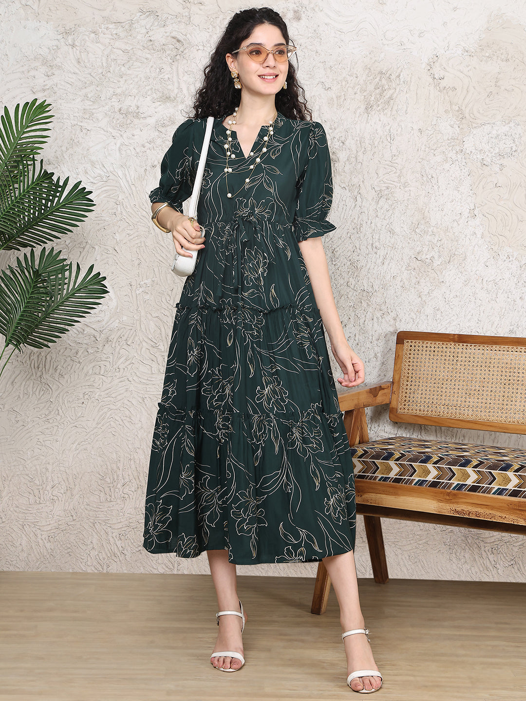 Woman wearing a dark green floral dress standing indoors with a neutral background